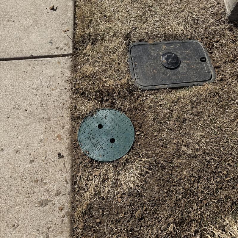 Pressure reducing valve cover in front yard dirt near sidewalk