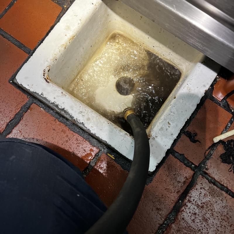 Floor sink drain clearing with hose flushing in restaurant