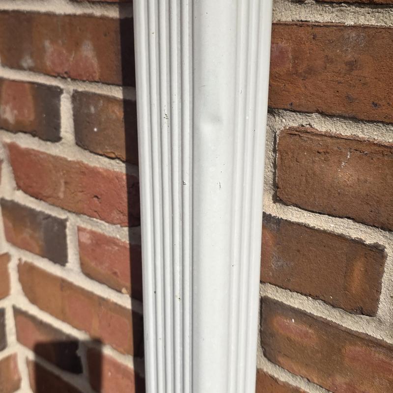 Downspout dent from hail damage on brick wall
