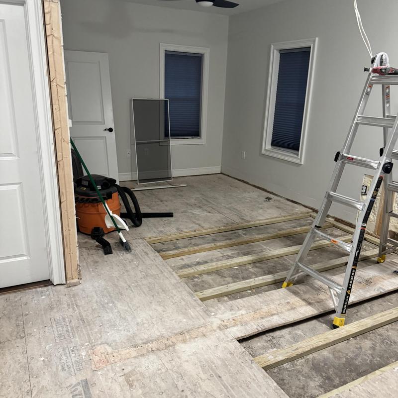 Hardwood floor installation with exposed joists and ladder