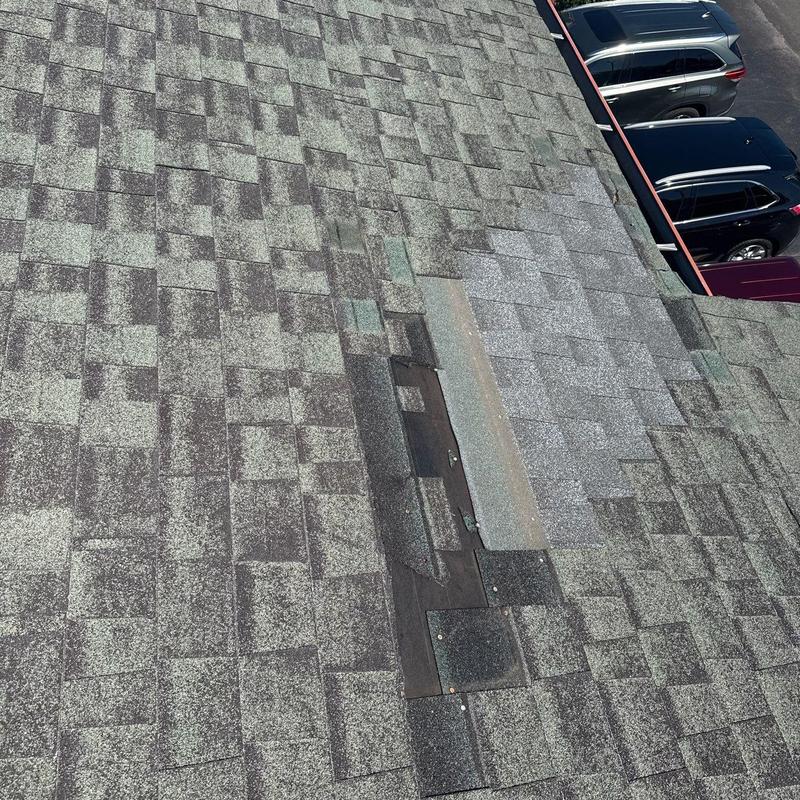 Asphalt shingle roof with patch and wear near parking lot