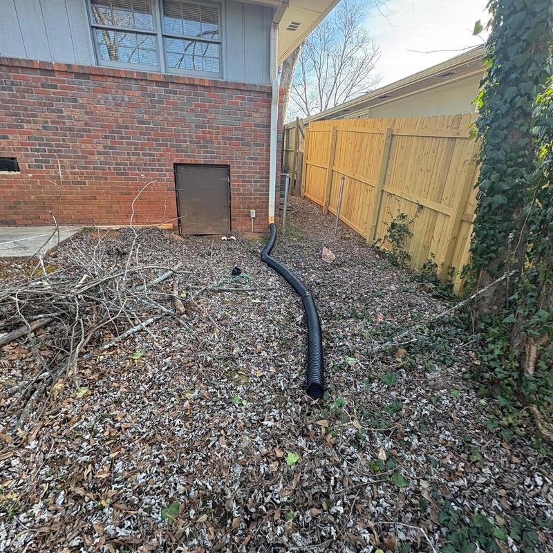 Downspout extension installed alongside brick house and fence