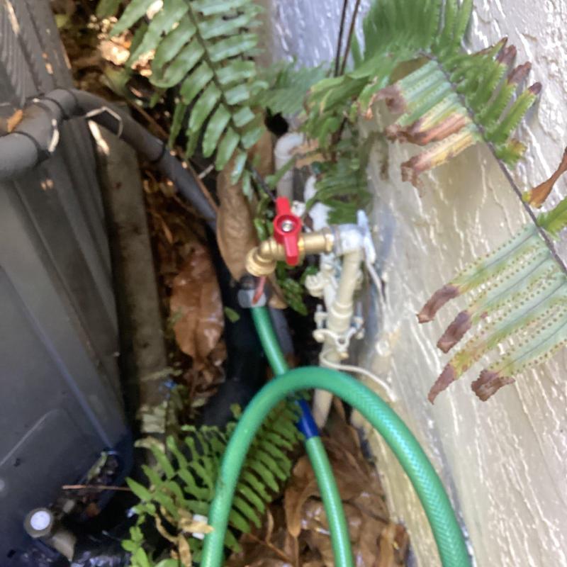 Hose bib with red handle and garden hose attached outdoors