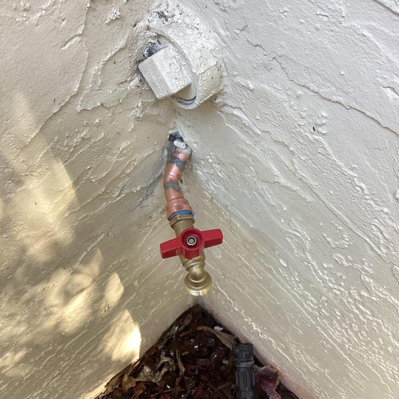 Hose bib with red valve handle on stucco wall