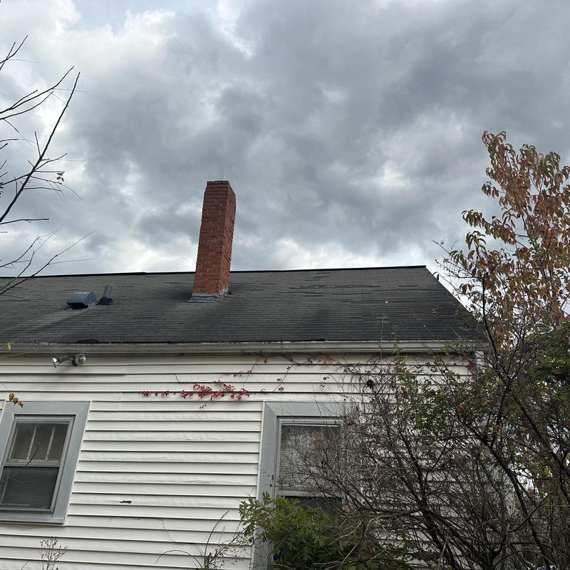 Asphalt shingle roof with chimney and vents under gray sky