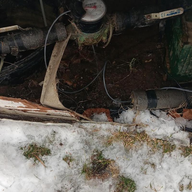 Water meter and frozen pipes exposed in snow-filled ground