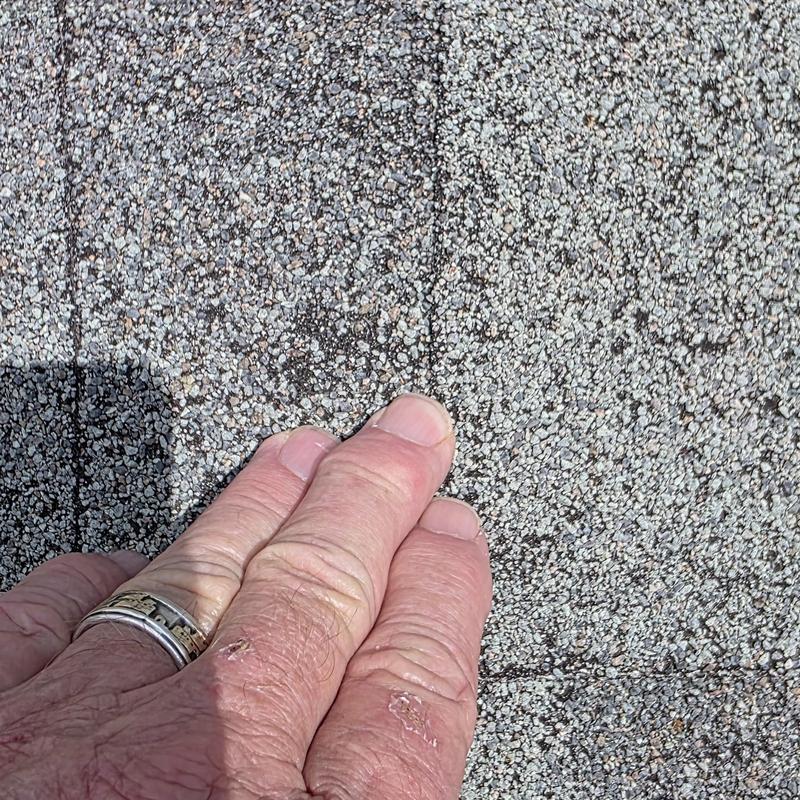 Asphalt roof shingles close-up with hail damage and hand