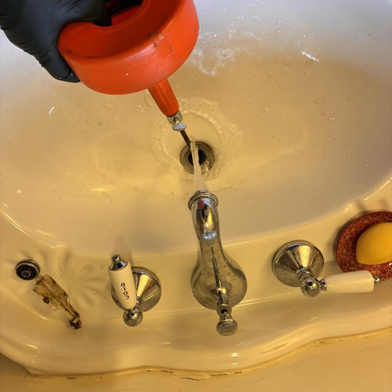 Pedestal sink drain clearing with plumbing auger