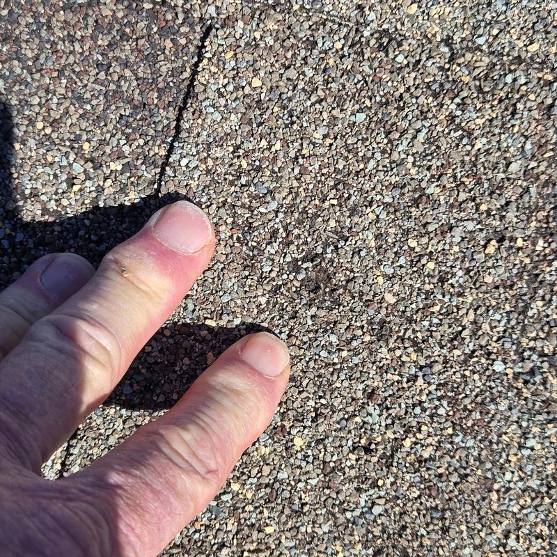 Asphalt shingle roof hail damage close-up with fingers