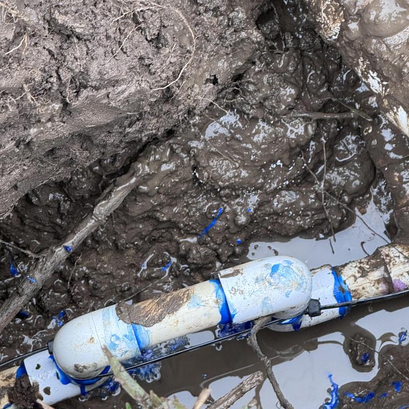 PVC water pipe with replaced elbow fitting in muddy hole