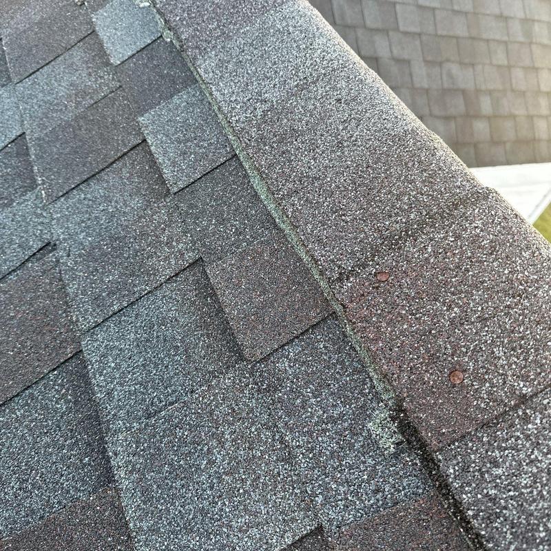 Asphalt shingle roof ridge with hail damage and rusted nails