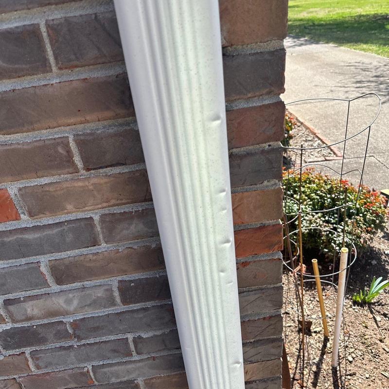 Downspout with visible dents on brick exterior wall