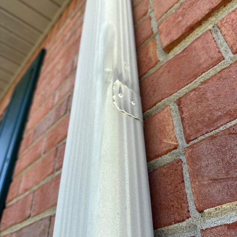 Metal downspout with dent and nail holes on brick wall