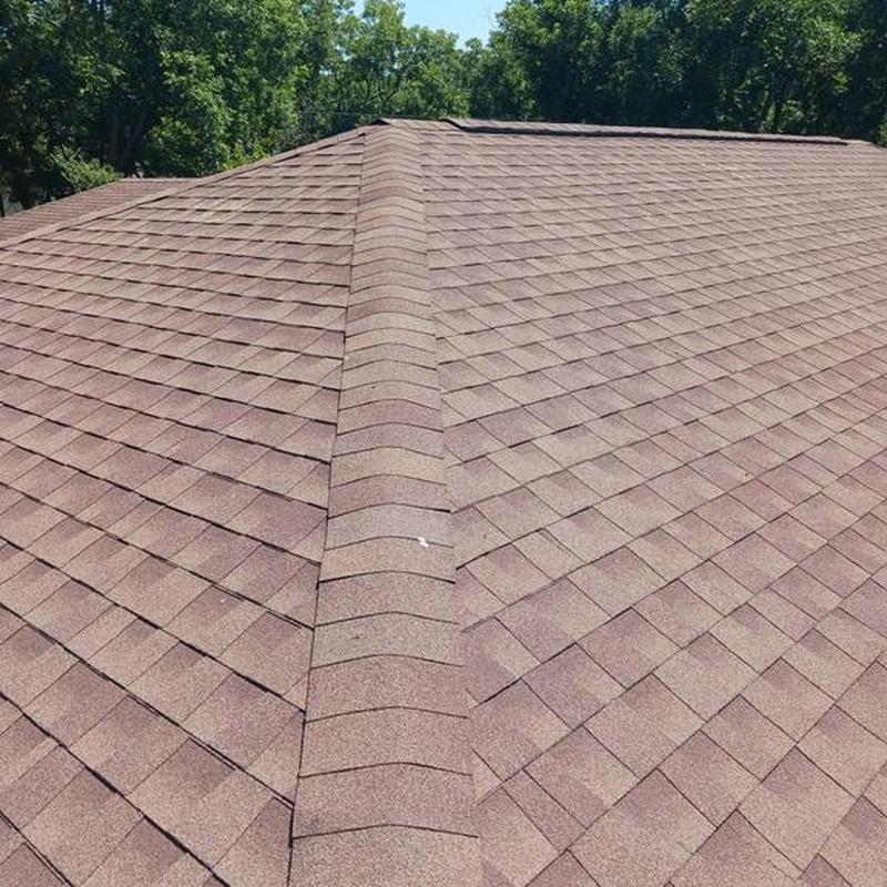 Asphalt shingle roof ridge with brown shingles under clear sky