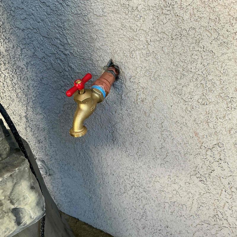 Outdoor hose bib with red handle valve installed on stucco wall