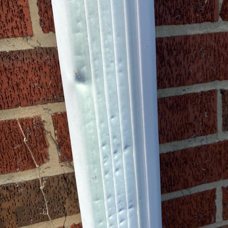 Downspout with hail impact dents on brick wall background