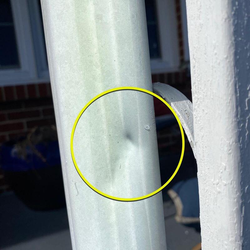 Metal downspout dent with circled hail damage