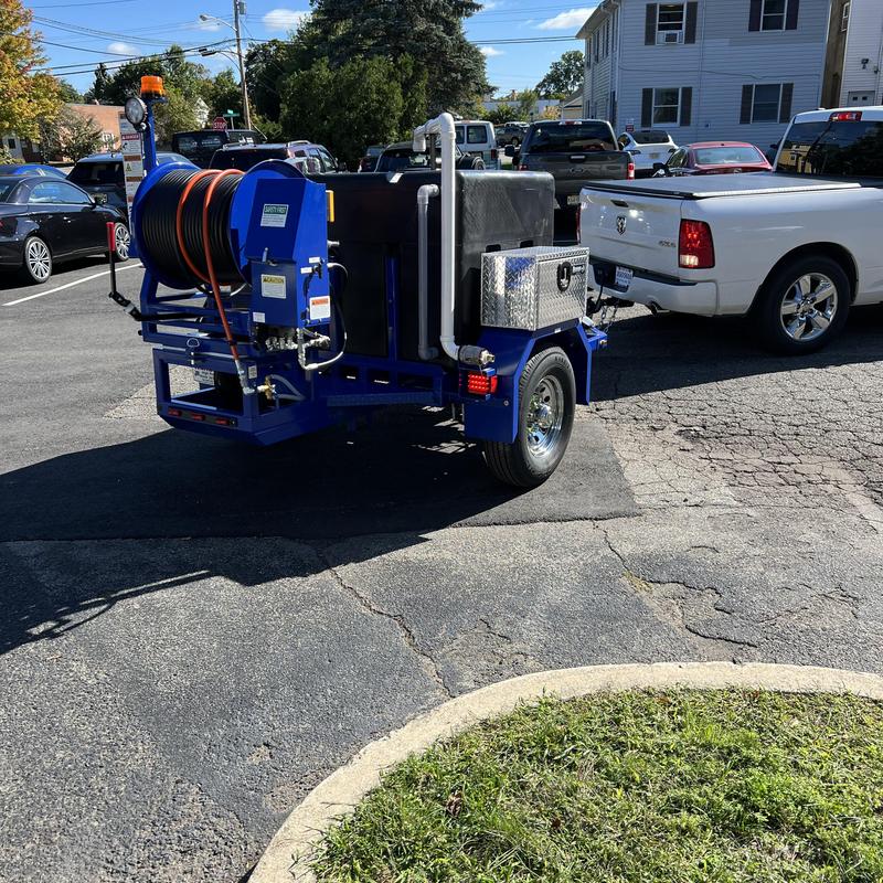 Sewer line jetter trailer hooked to white truck in parking lot