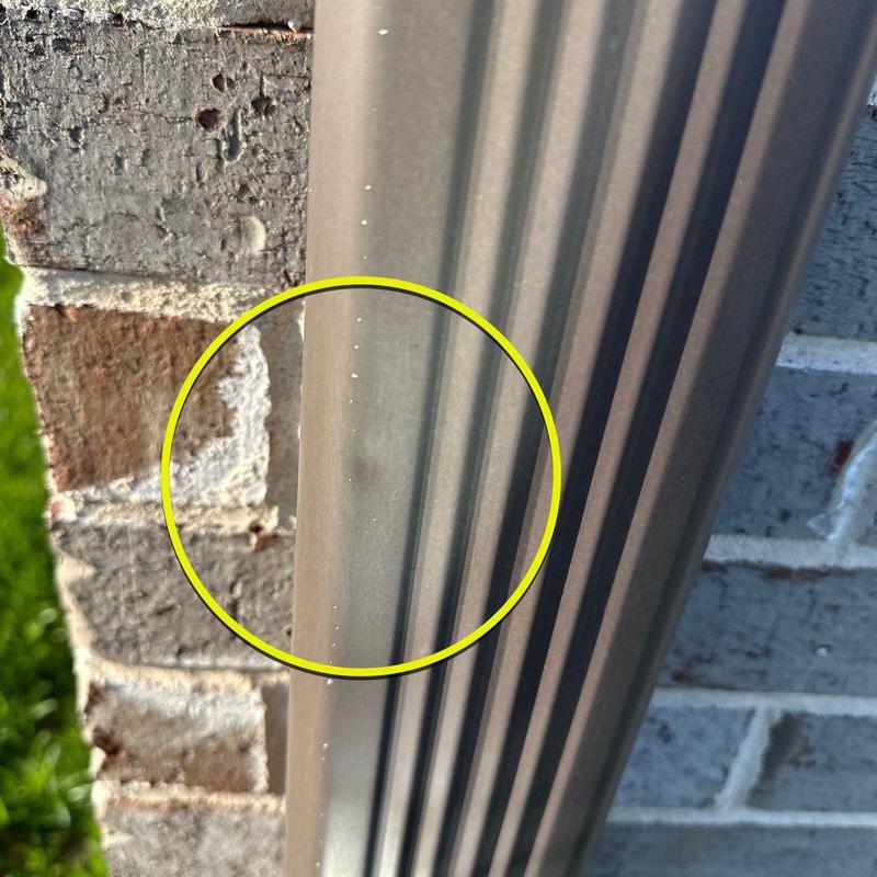 Metal gutter dent from hail impact on brick wall background
