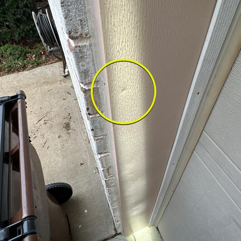 Siding panel dent marked in yellow circle near garage door