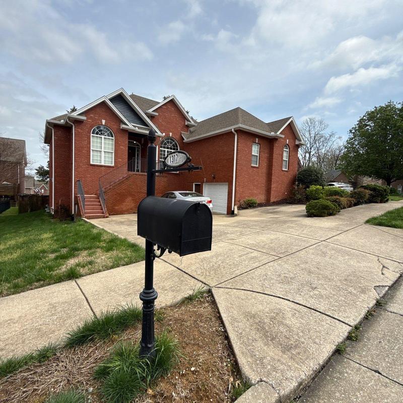 Mailbox post and black mailbox by driveway and brick house