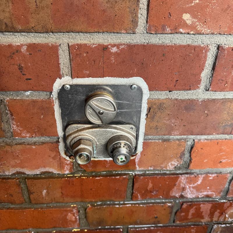 Commercial hose bib with metal wall plate on brick wall