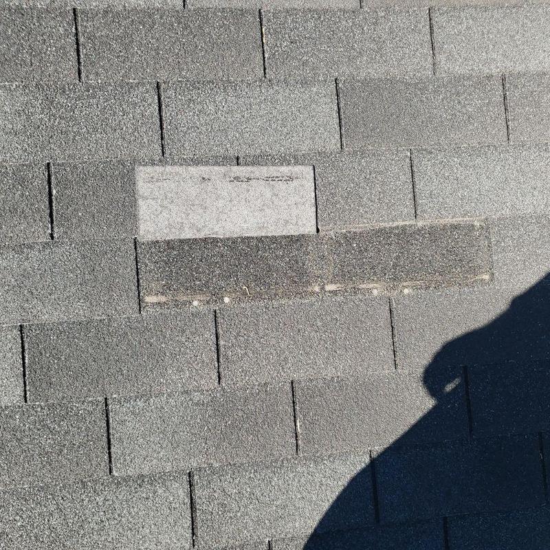 Roof shingles with visible wind damage and missing granules Roof shingles with visible wind damage and missing granules