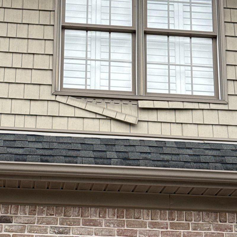 Asphalt shingle roof with damaged siding panel below window