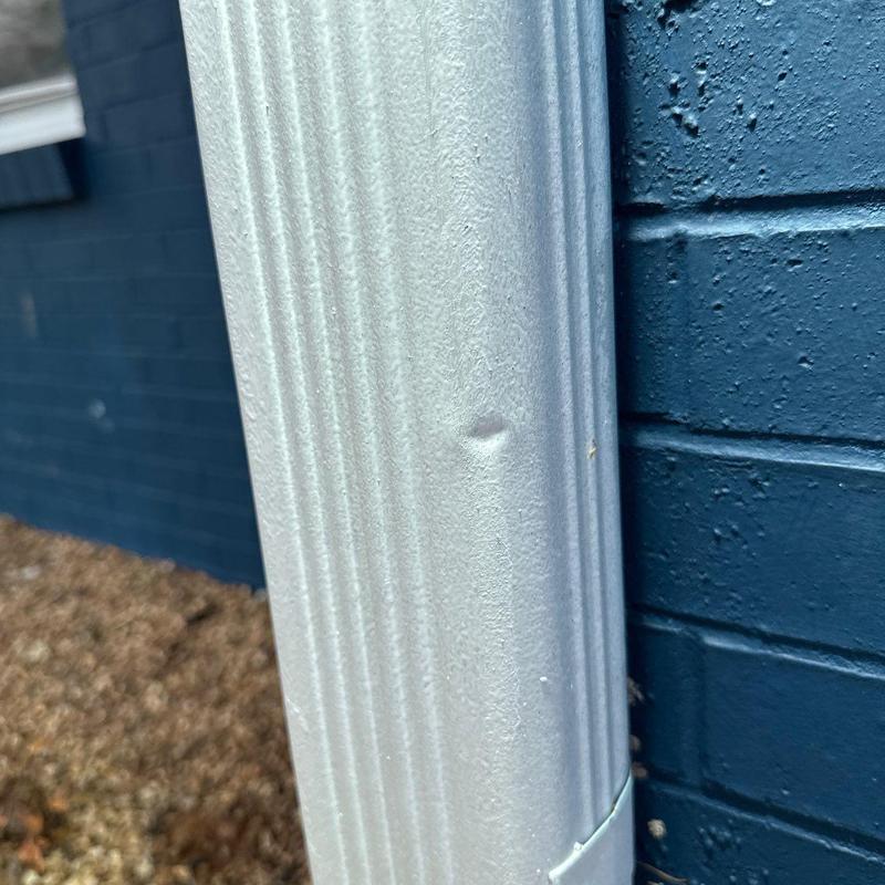 Metal downspout with a dent from hail damage