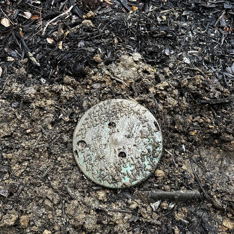 Water meter cover partially buried in dirt and mulch