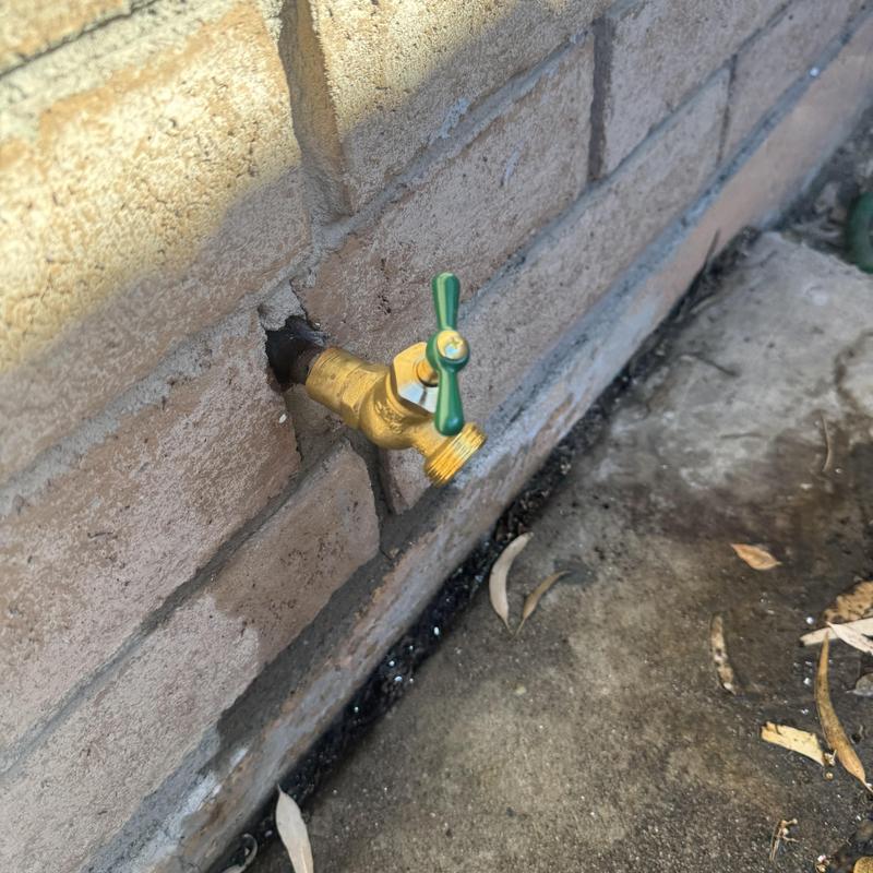 Hose bib with green handle on exterior brick wall