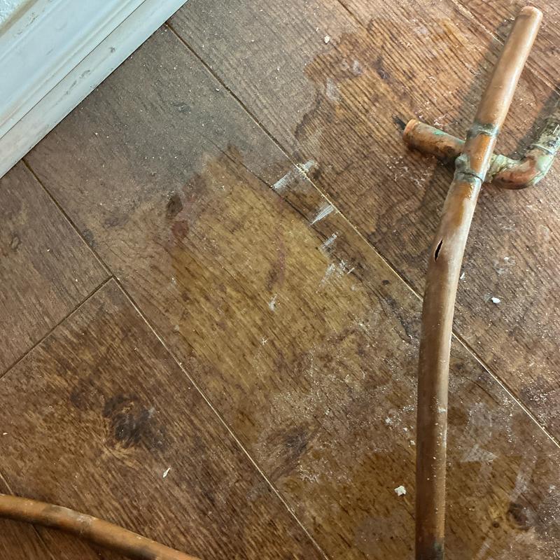 Damaged copper pipe with corrosion and cracks on wood floor