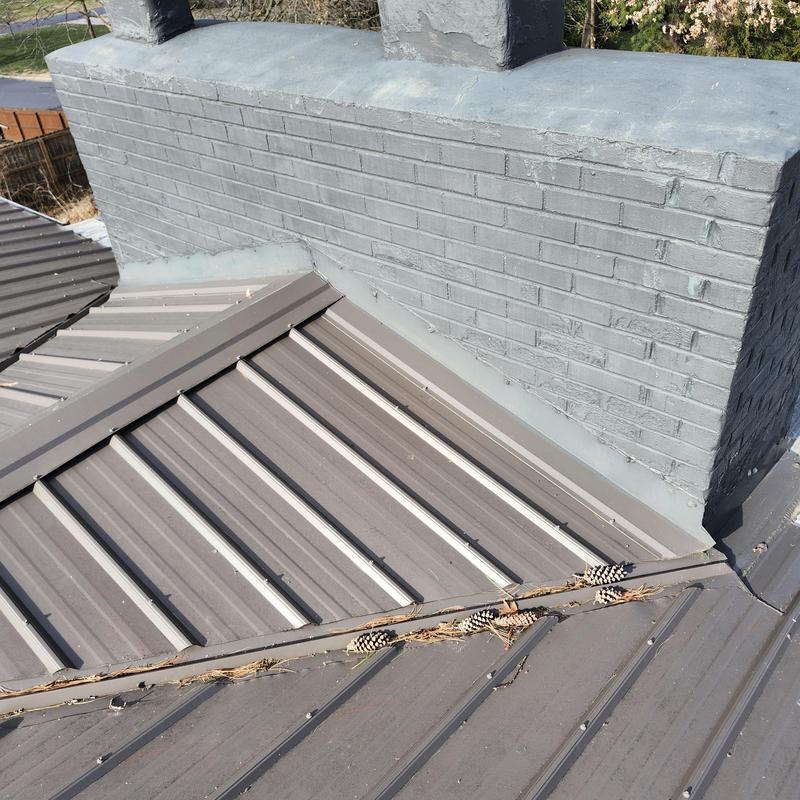 Metal roof valley with debris near chimney flashing