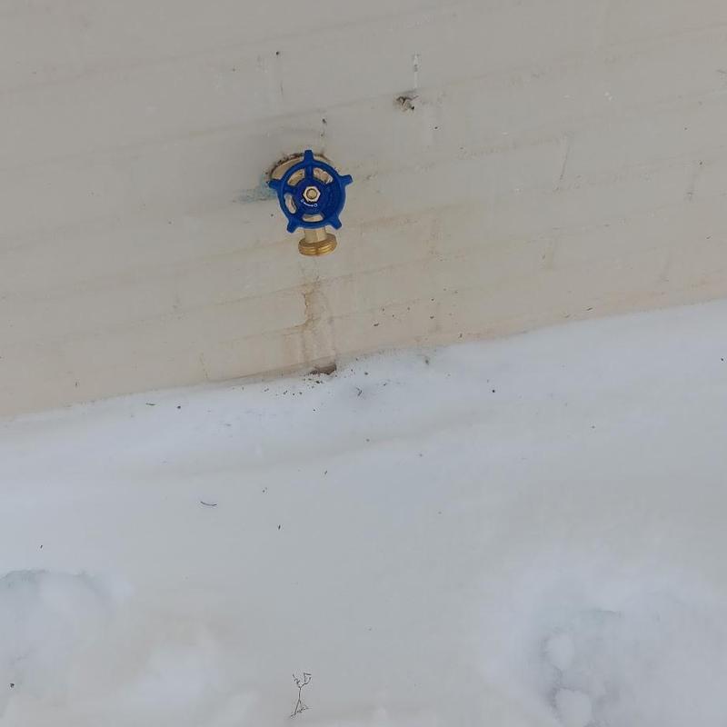 Outdoor water shutoff valve on exterior wall with snow