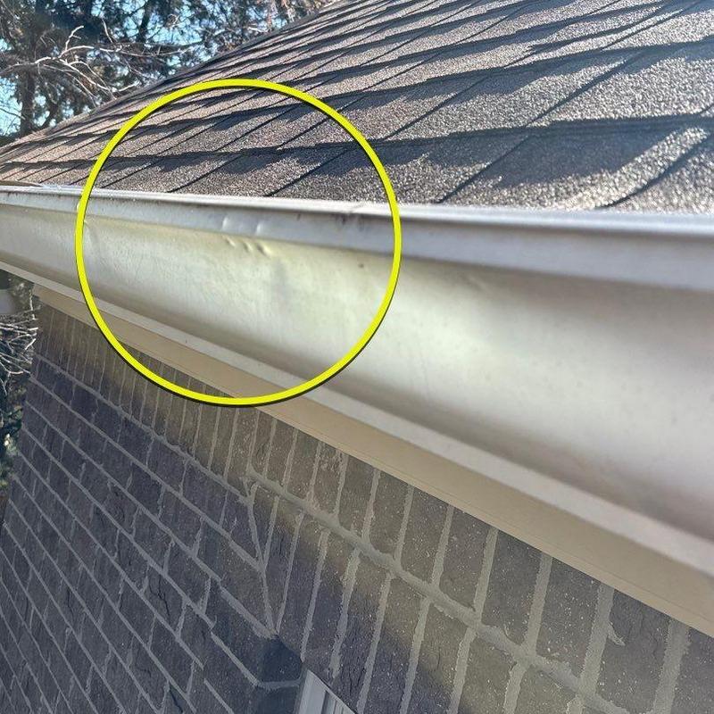 Gutter dent damage from hail with roof shingles above