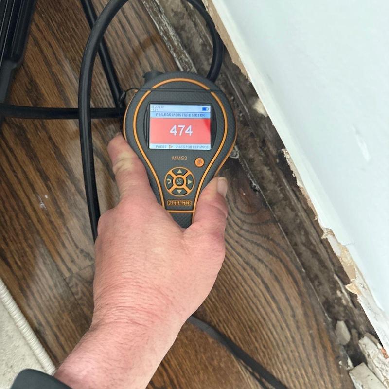 Floor moisture meter detecting water damage near baseboard
