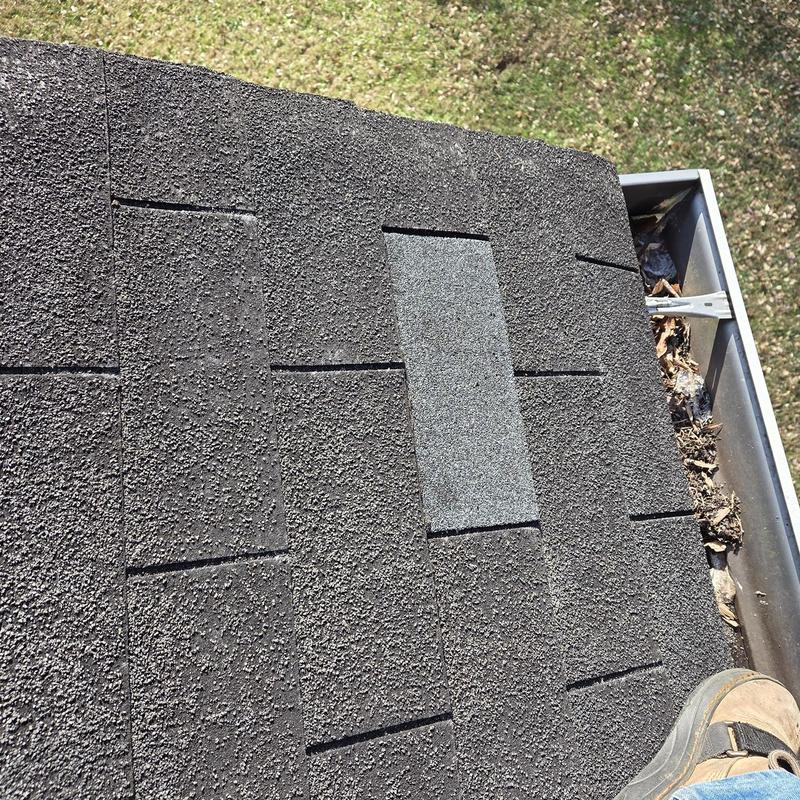 Asphalt shingles with replaced damaged shingles near gutter