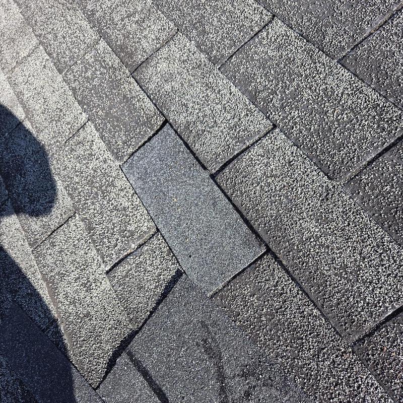 Roof shingles with one replaced darker shingle nearby