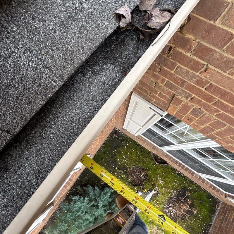 Gutter with debris and measuring tape on roof edge