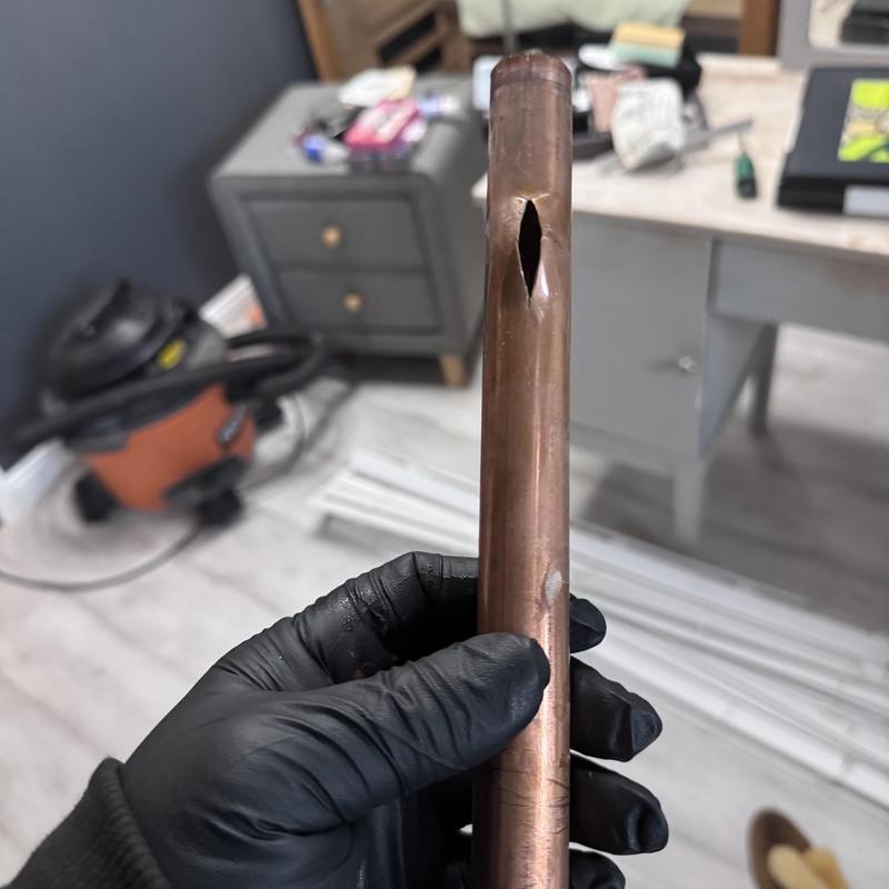 Copper pipe with burst hole held by gloved hand