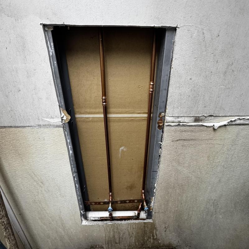 Copper plumbing pipes with shutoff valves behind wall panel