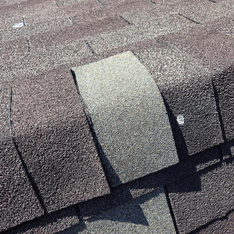 Damaged asphalt shingle on residential roof ridge