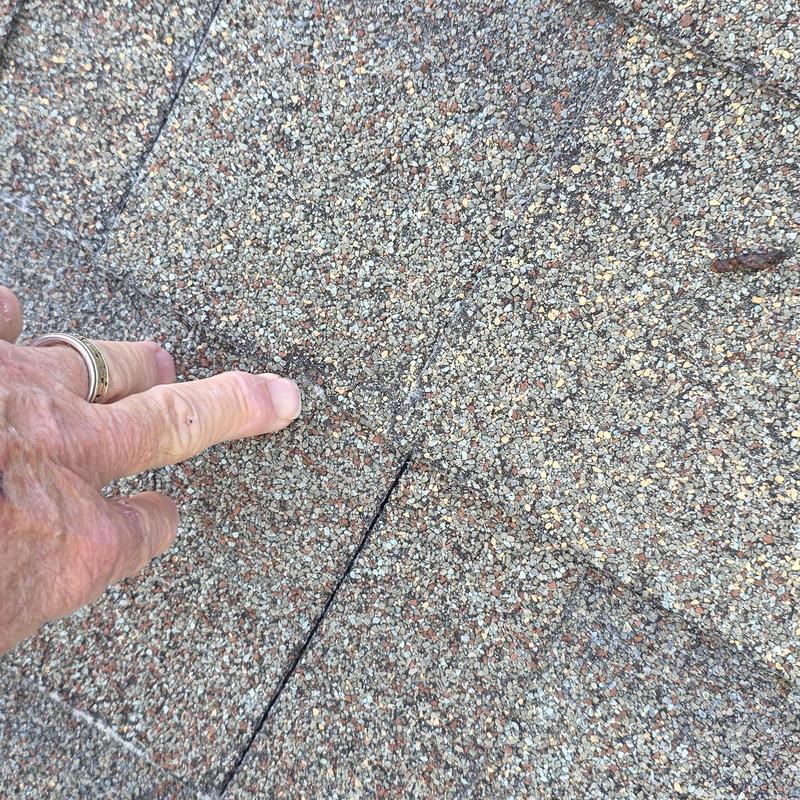 Asphalt roof shingle crack inspection with finger pointing
