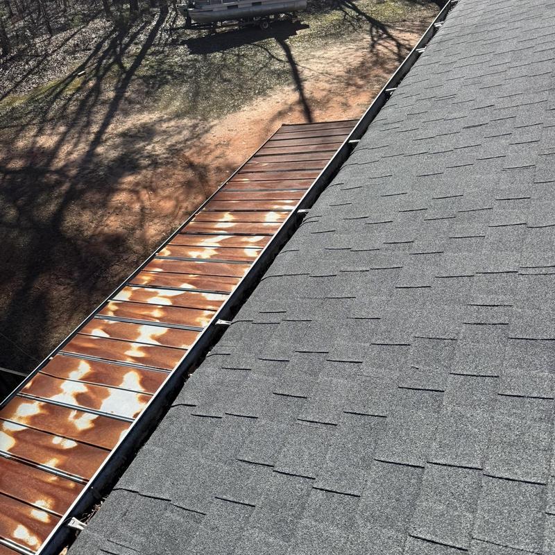 Metal gutter with rust spots alongside asphalt roof shingles
