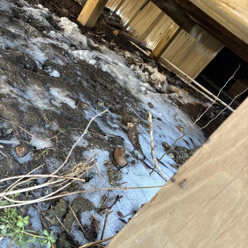 Frozen pipe under home with ice and dirt debris