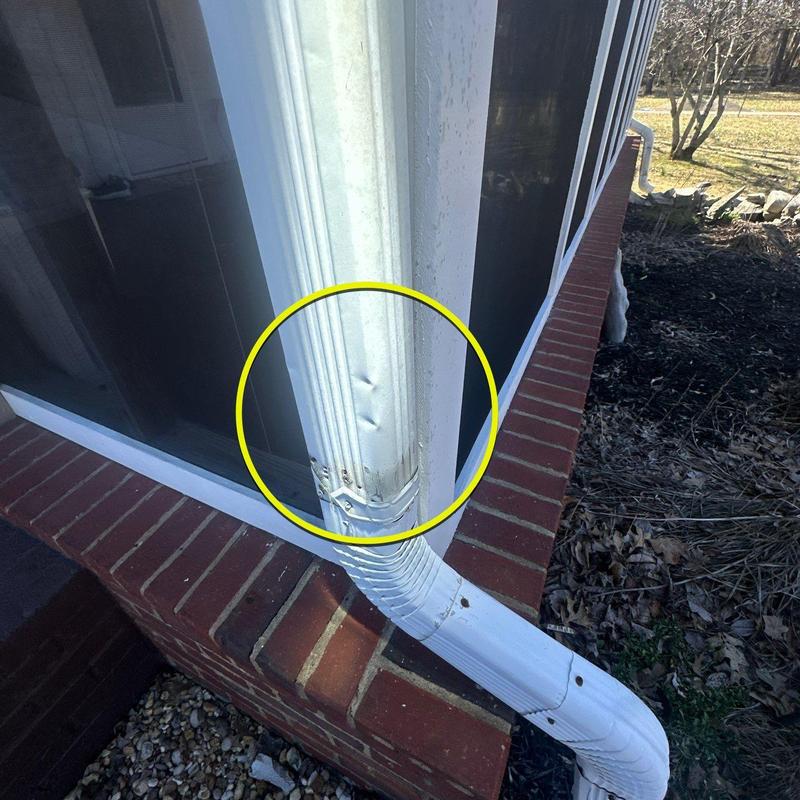 Downspout dent with circled damage on white gutter system
