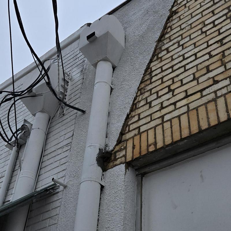 Roof drainpipe with wall damage near brick facade
