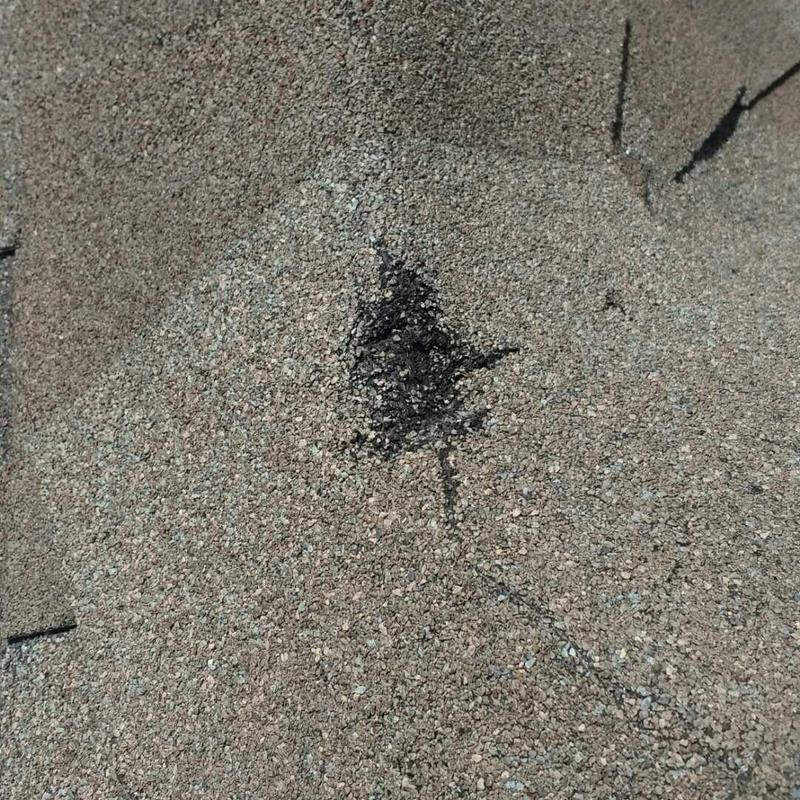 Roof shingle hail damage with black impact mark close-up
