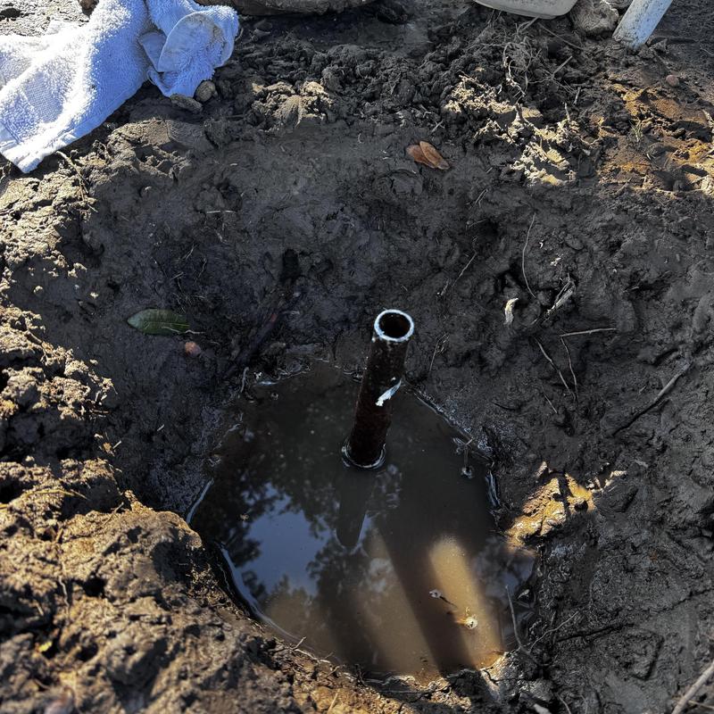Galvanized water pipe exposed in muddy ground hole