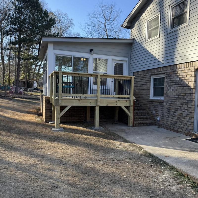 Attached wooden deck with railing and enclosed patio